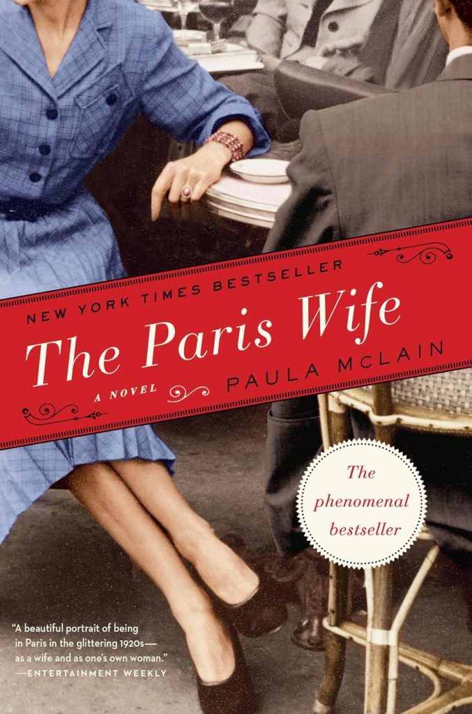 The cover of Paula Mclain's book The Paris Wife. It features a woman in a blue dress and the back of a man in a suit sitting at a cafe table.